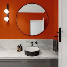 a bathroom with orange walls and marble counter tops, round mirror on the wall above the sink