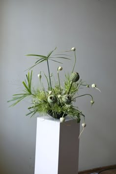 a white vase filled with flowers on top of a hard wood floor next to a wall