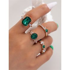 a woman's hand holding three rings with emeralds and diamonds