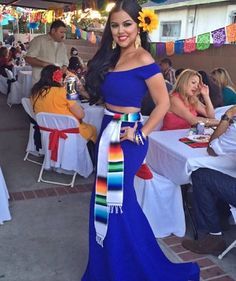 a woman in a blue dress standing next to a table with white tables and chairs