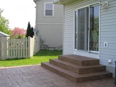 a patio with steps leading up to the back door and side yard in the background