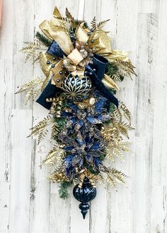 a blue and gold christmas wreath hanging on the side of a white wooden wall with ornaments