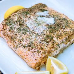 a white plate topped with fish covered in herbs and lemon wedges next to a slice of lemon