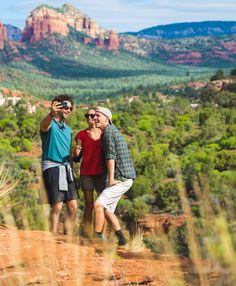 two men and a woman standing on top of a mountain taking pictures with their cell phones