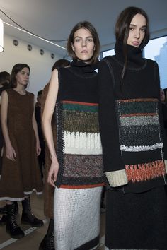 two women standing next to each other wearing sweaters