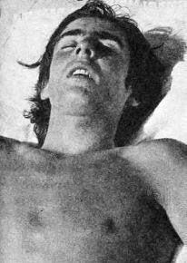 an old photo of a man with no shirt on laying in bed looking up at the sky