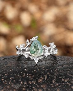 a ring with a green and white stone in the center on top of a rock