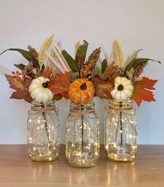 three mason jars filled with pumpkins, leaves and other autumn decorations on a table