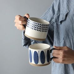 a person holding two coffee mugs in one hand and another cup in the other