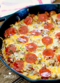 a pizza with pepperoni and cheese in a pan on a wooden table next to a fork