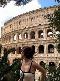 a woman standing in front of the colossion looking at the sky and trees