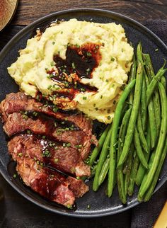 steak, mashed potatoes and green beans on a black plate with buttered bread