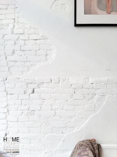 a white brick wall with a painting hanging on it's side next to a pair of shoes