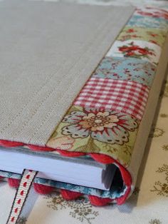 an open book on top of a table covered in flowers and fabric ribbones, with the cover partially closed