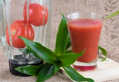 a smoothie in a glass next to a blender filled with tomatoes