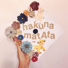 a hand holding up a white graduation cap with the words hakuna matata on it