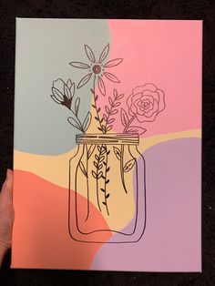 a hand holding up a painting with flowers in a mason jar on a pink and blue background