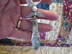 a hand holding a small silver spoon with an angel charm on it