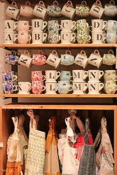 many tea cups and mugs are on display in a cabinet with wooden shelves above them