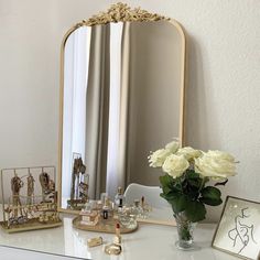 a white dresser topped with a vase filled with flowers next to a mirror and other items