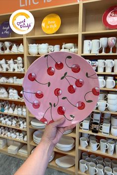 a person holding up a pink plate with cherries on it in front of shelves