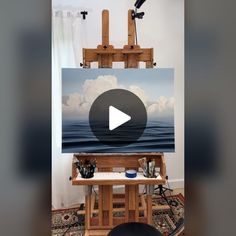 an easel is sitting in front of a painting with clouds and water on it