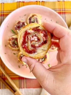 a person holding a pastry in their hand on top of a pink plate with chopsticks