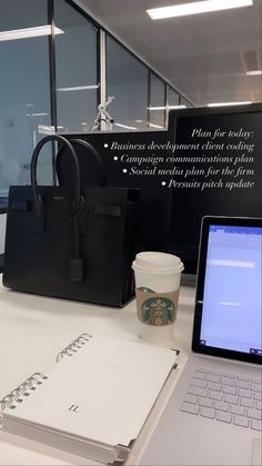 an open laptop computer sitting on top of a white desk next to a cup of coffee