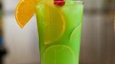 a tall glass filled with green liquid and orange slices