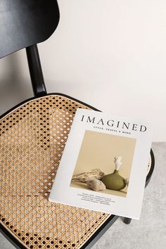 a magazine sitting on top of a wooden chair next to a black chair with a green vase