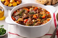 a bowl of beef stew with carrots, potatoes and bread