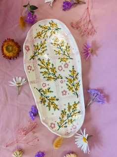 an oval platter with yellow and purple flowers surrounding it on a pink tablecloth