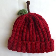 a red knitted hat with a green leaf on it's tip, sitting on a white surface