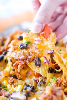 a hand holding a cheesy casserole with black beans and corn