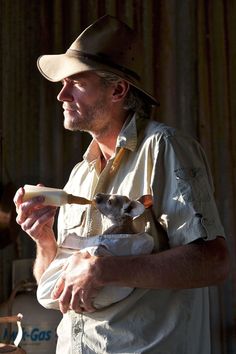 a man in a hat holding a small animal while standing next to a metal container