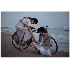 a man and woman on the beach with a bicycle in front of them, both touching hands