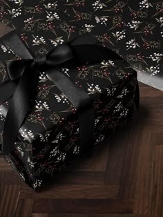 a gift wrapped in black paper with a large bow on it's head and sitting on top of a wooden floor