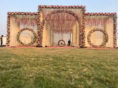 an outdoor stage set up for a wedding ceremony with flowers and wreaths on it