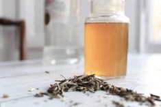 a glass bottle filled with liquid sitting on top of a white table next to a pile of leaves