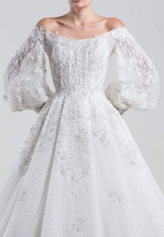 a woman wearing a white wedding dress with long sleeves and an off the shoulder design