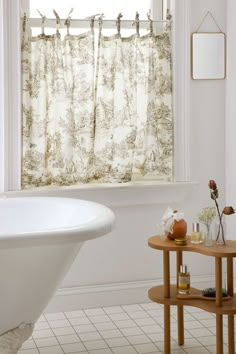 a white bath tub sitting under a window next to a table with flowers on it