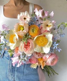 a woman is holding a bouquet of flowers in her jeans shorts and white tank top