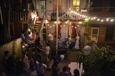 a group of people standing around in front of a building with lights strung from the roof