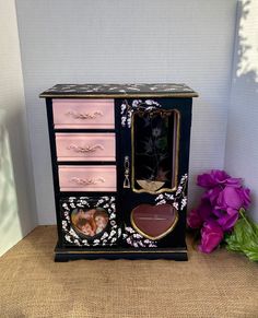 Adorable Heart Jelwerybox with a picture holder. This two-tone petite jewelry armoire has enough space for all your jewelry and a heart picture holder. I am excited to present this beautiful gift, which includes a jewelry box designed with two-tone colors and hand-painted lilac flowers. Everything in my shop has been up-cycled and previously owned. Please expect some imperfections. There might be present some visible stains. I take great care and put in much love to transform old and unwanted furniture into desirable pieces once again. I live in Santa Rosa, CA, and work in my garage. My inspiration comes from the French Country/Province styles. I aim to make everything in my store for you with various original floral hand-painting, wooden applique, or gold leaf applications. And depending Standing Jewelry Box, Heart Jewelry Box, Jewelry Box Makeover, Petite Jewelry, Whimsical Painted Furniture, Jewelry Box Design, Painted Jewelry Boxes, Antique Wax, Picture Holders