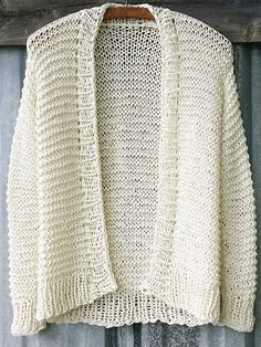 a white knitted sweater hanging on a wooden hanger with an old door in the background