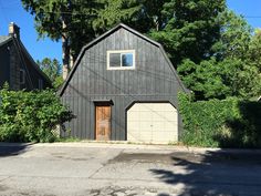 a black barn with two garages on the side and trees in the back ground