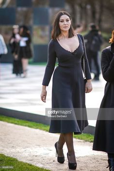 a woman in a black dress is walking down the street with her hand on her hip