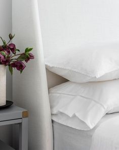 a vase with flowers sitting on top of a bed next to white sheets and pillows