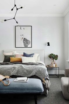 a bedroom with white walls and gray carpeted flooring, a bed in the center