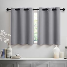 two gray curtains hanging on the side of a wall next to a vase with flowers